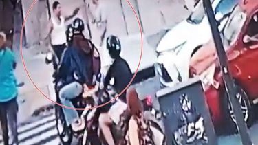 Los dos hombres peleando en l a vereda, mientras transeúntes y motociclistas los miran.