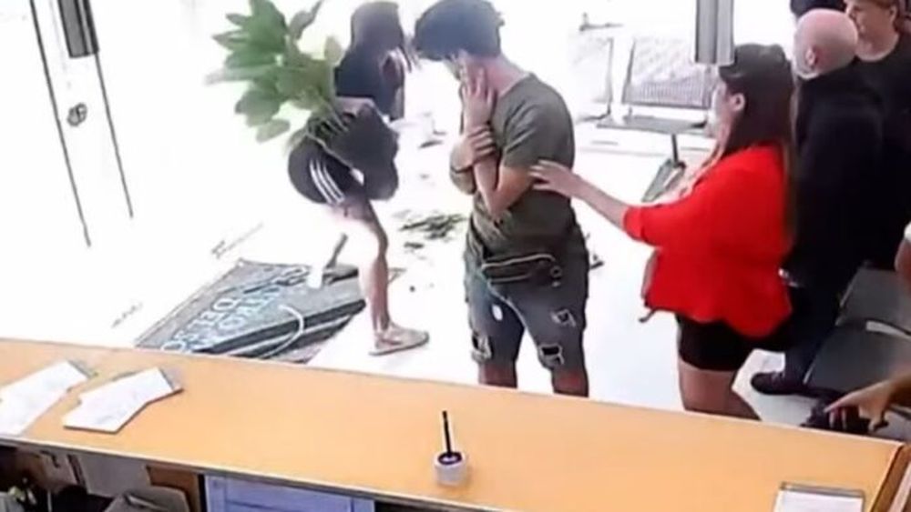 Momento en el que la mujer se prepara para arrojar la maceta contra el vidrio de la clínica. (Captura de video)